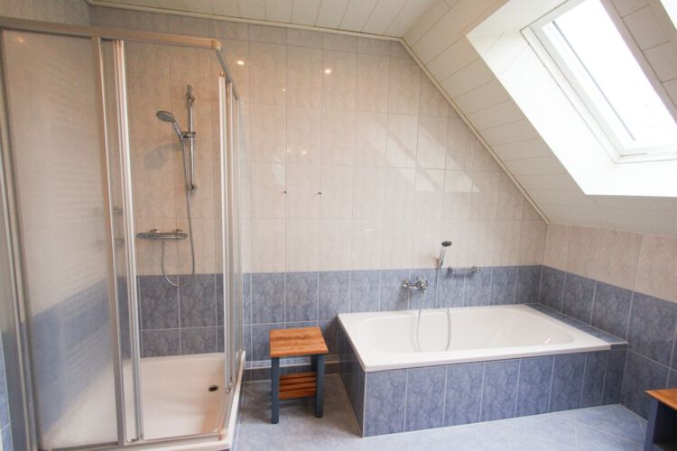 gefliestes Badezimmer mit Badewanne und Dusche, kleiner Holzhocker, Dachfenster