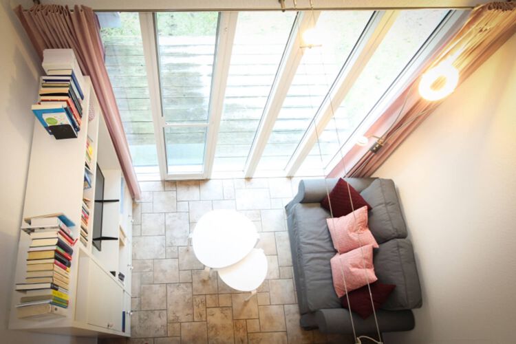 Blick vom OG in den Wohnbereich im Erdgeschoss mit Couch, Couchtisch, Anbauwand und Flatscreen-TV, Zugang zur Terrasse