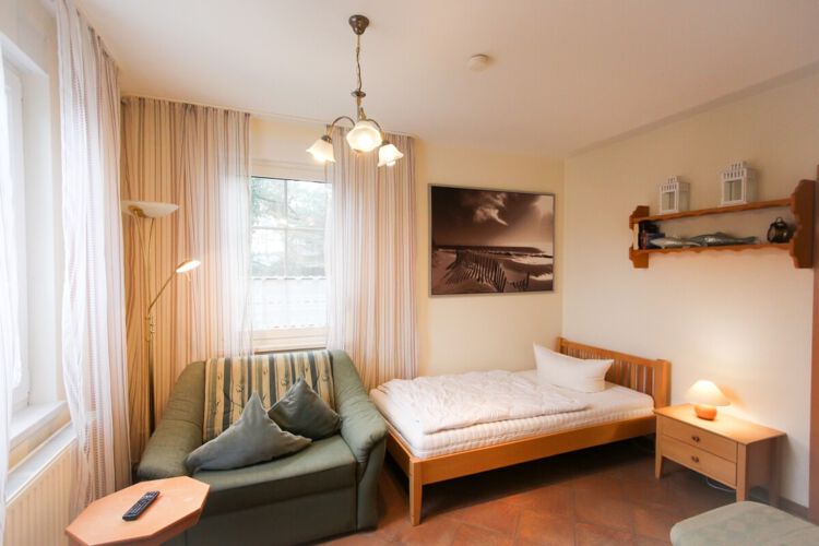 lichtdurchfluteter, gefliester Wohnbereich mit einem Einzelbett und einem komfortablen Schlafsessel, Couchtisch, Nachttisch und Lampe