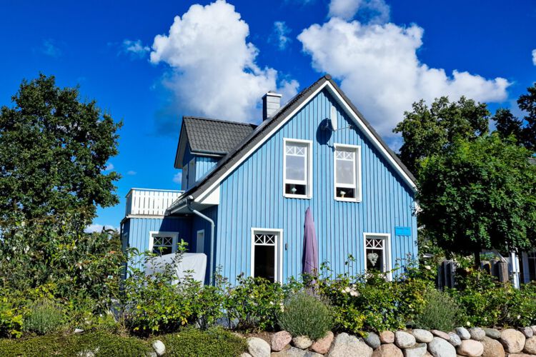 das blaue Haus ist umgeben vom satten gruen mit einer bepflanzten Steinmauer