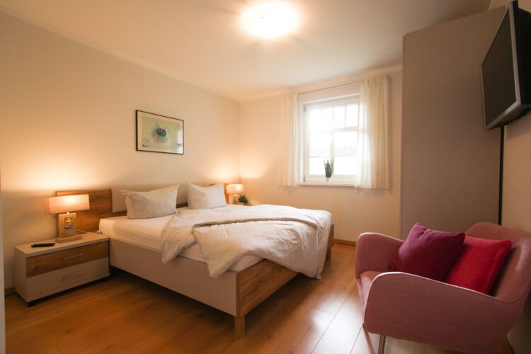 ein Schlafzimmer in Wohlfuehlatmosphaere mit Doppelbett auf einem Laminatfussboden mit Kleiderschrank, Flatscreen-TV, Fenster in den ruhigen Garten